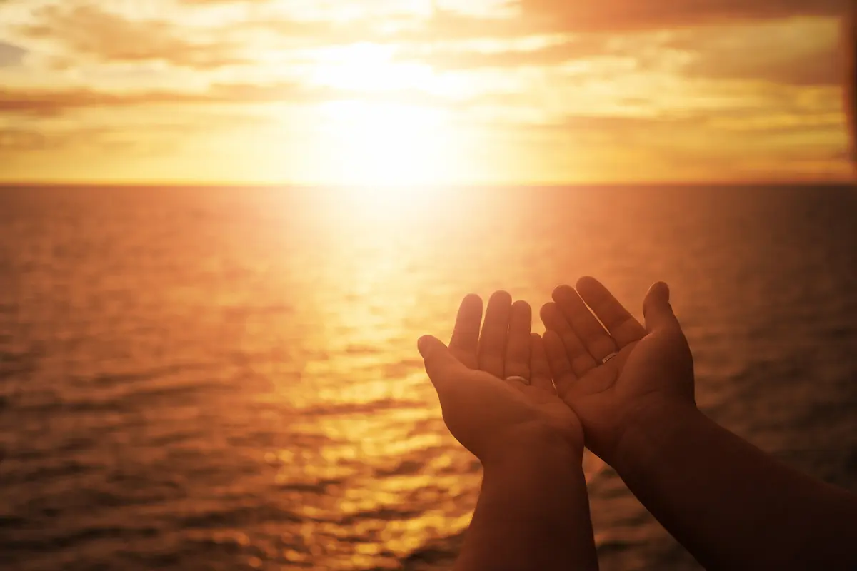 Mãos abertas em direção ao mar ao pôr do sol